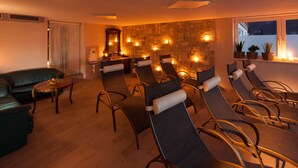 A room with a stone wall, a sofa, a massage table, and a window with plants. - Krepperhütte (Volders)