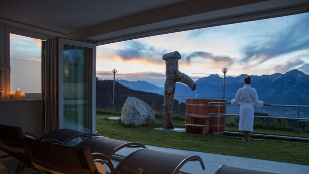 A modern outdoor seating area with a view of mountains and a wooden sculpture. - Krepperhütte (Volders)