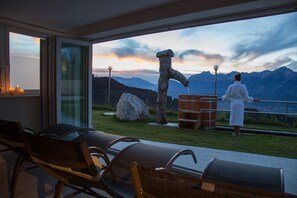 Un espace extérieur moderne aménagé avec des sièges, offrant une vue sur les montagnes et agrémenté d’une sculpture en bois.