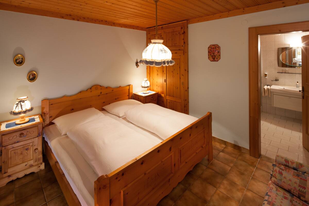 Un lit en bois dans une chambre, avec une table de chevet, une lampe et un miroir au-dessus du lavabo.