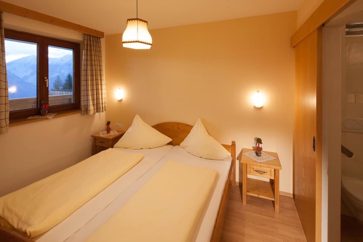 Une chambre avec deux lits, une table de chevet, une commode, une fenêtre avec des rideaux et une vue sur les montagnes.
