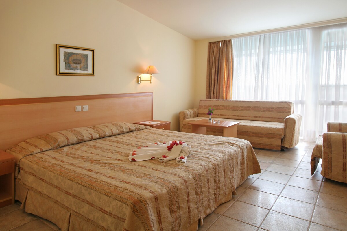 Habitación de hotel con una cama grande, un sofá, una mesita y una lámpara de pared.