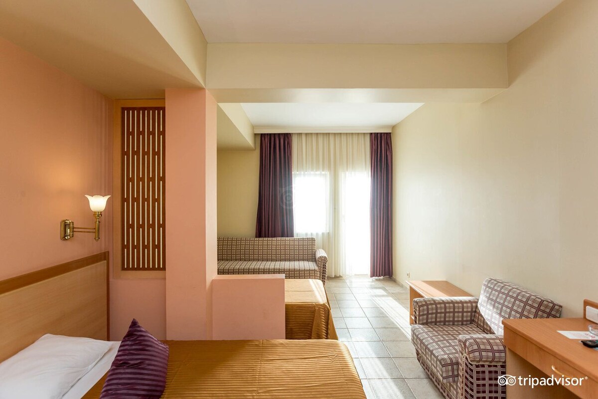Habitación de hotel con cama, sofá, una mesita y vista a otra habitación con ventana.