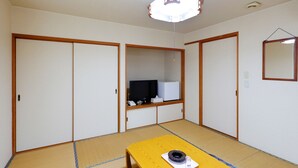 A traditional Japanese room with tatami flooring, a low wooden table, a television, and sliding doors. - Tabist Rays Hotel Yakata (Miyazaki)
