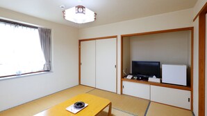 A room with tatami flooring, a wooden table with a tray, a television on a shelf, and a sliding door. - Tabist Rays Hotel Yakata (Miyazaki)