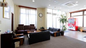 A lobby with leather sofas, a reception desk, a clock, and a vending machine. - Tabist Rays Hotel Yakata (Miyazaki)
