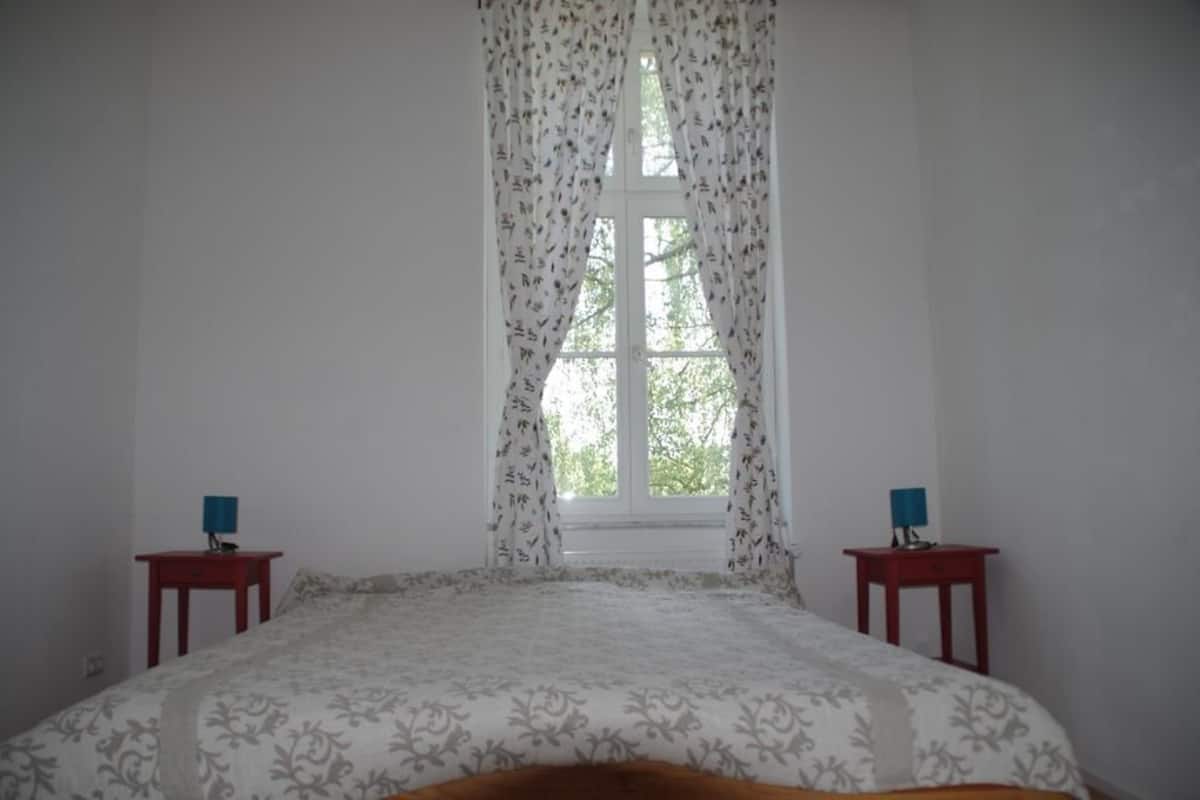Ein Schlafzimmer mit einem Bett, zwei Nachttischen und einem Fenster mit Vorhängen.