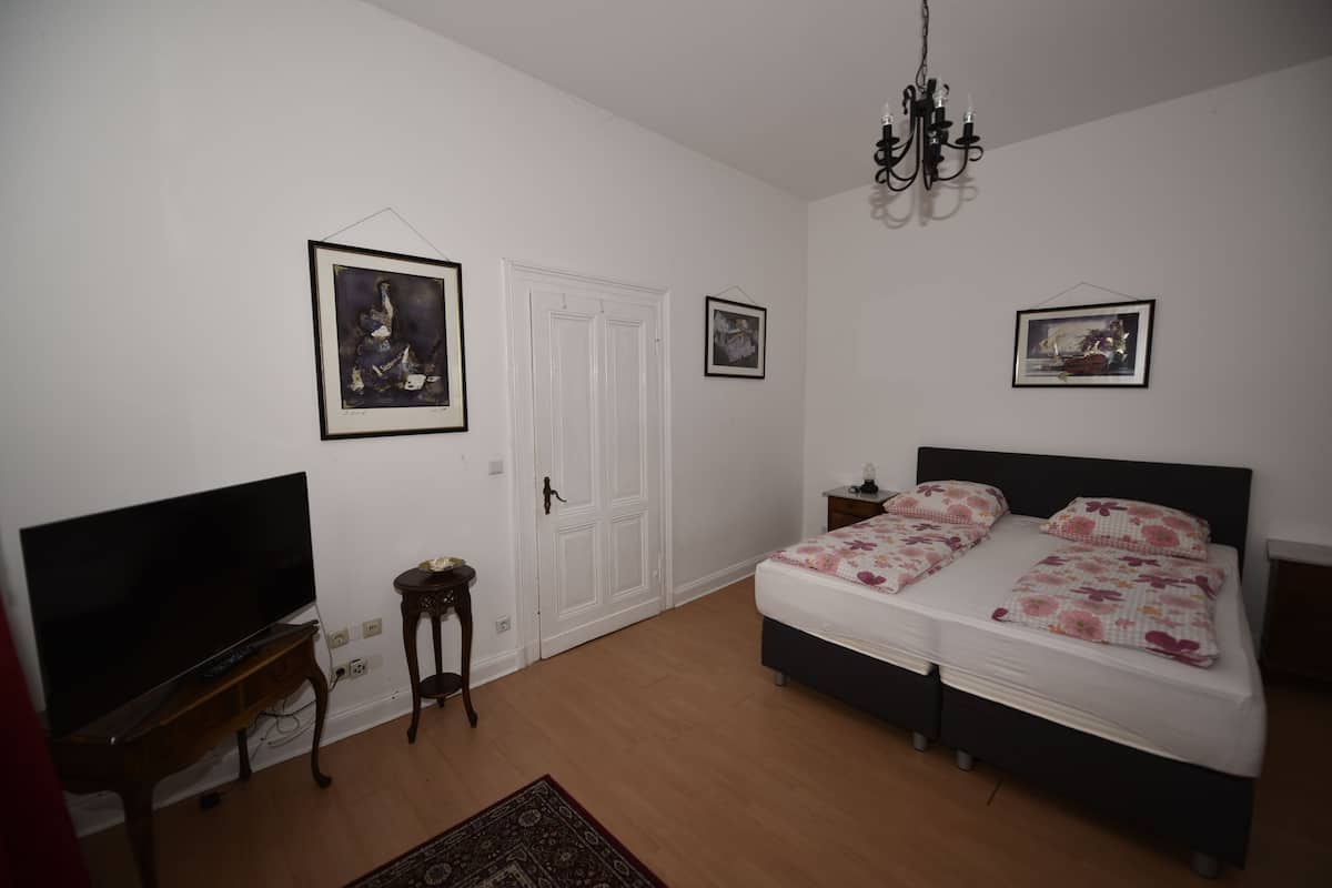 Ein Schlafzimmer mit einem Bett, einem Fernseher, einer Chandelüster und gerahmten Bildern an der Wand.