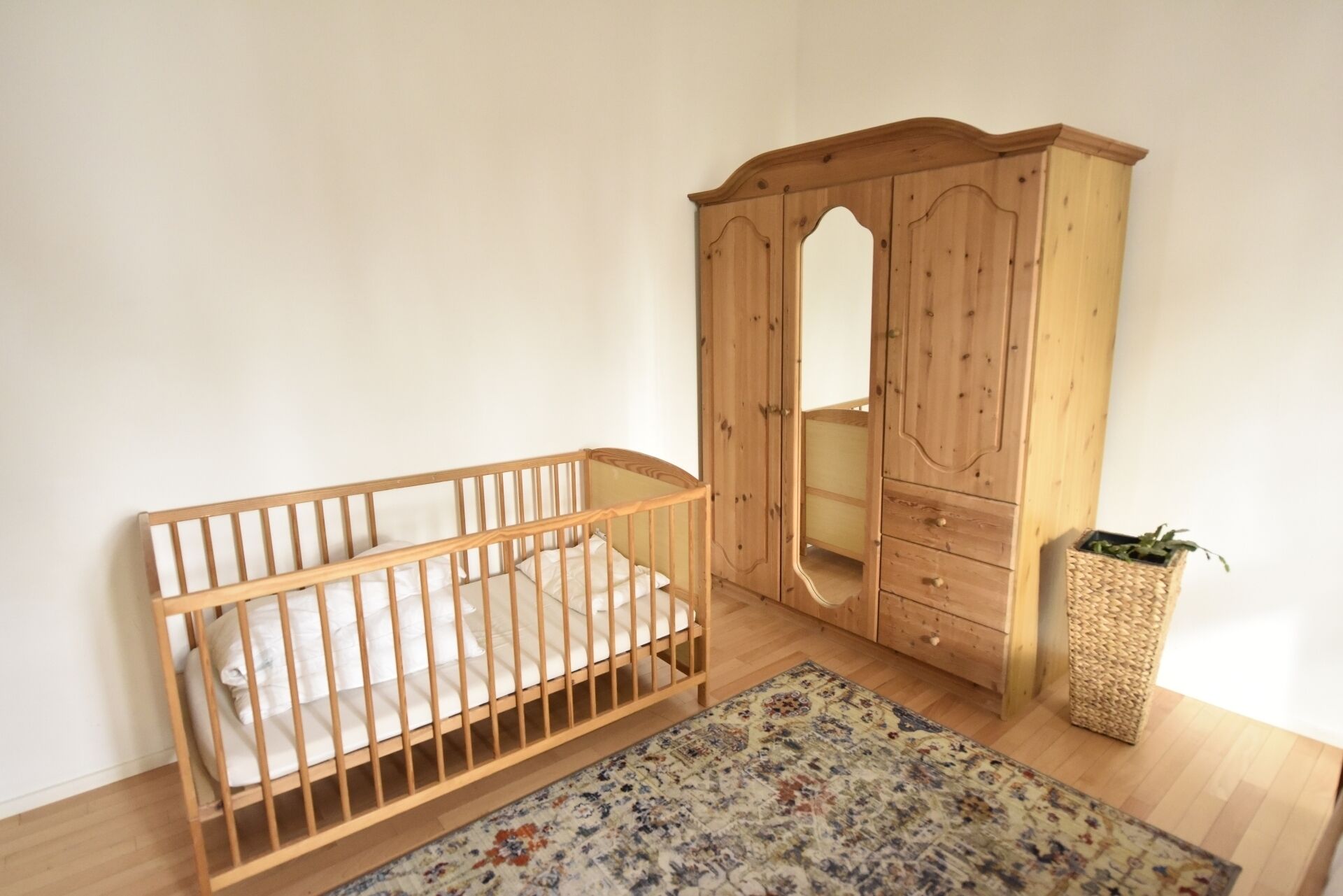 Una habitación con una cuna de madera, un armario y una cesta de mimbre.
