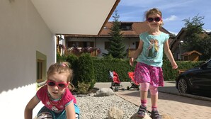 Deux enfants jouent près d’un bâtiment dont le toit est recouvert de tuiles, et dans un jardin où se trouve une poussette.