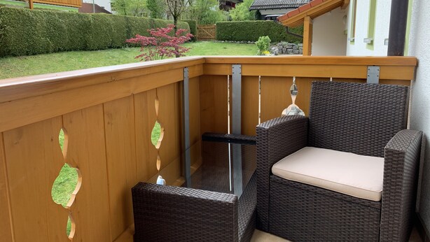 Un balcon d’angle agrémenté de meubles en osier et d’une rambarde en bois.