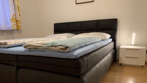 Une chambre à coucher avec un lit marron foncé, une table de chevet blanche et une lampe de chevet.