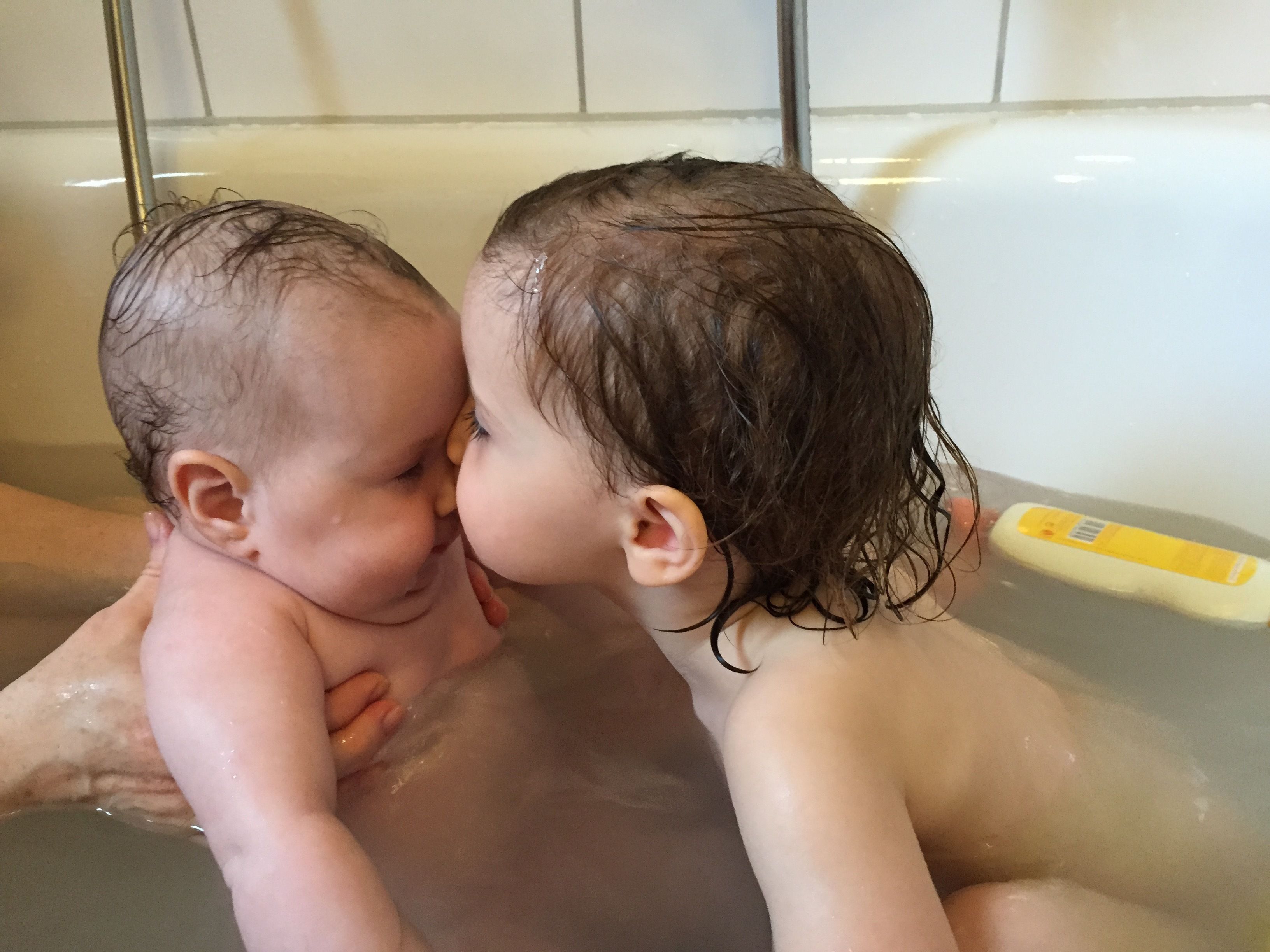 Dos niños en una bañera con una botella amarilla.