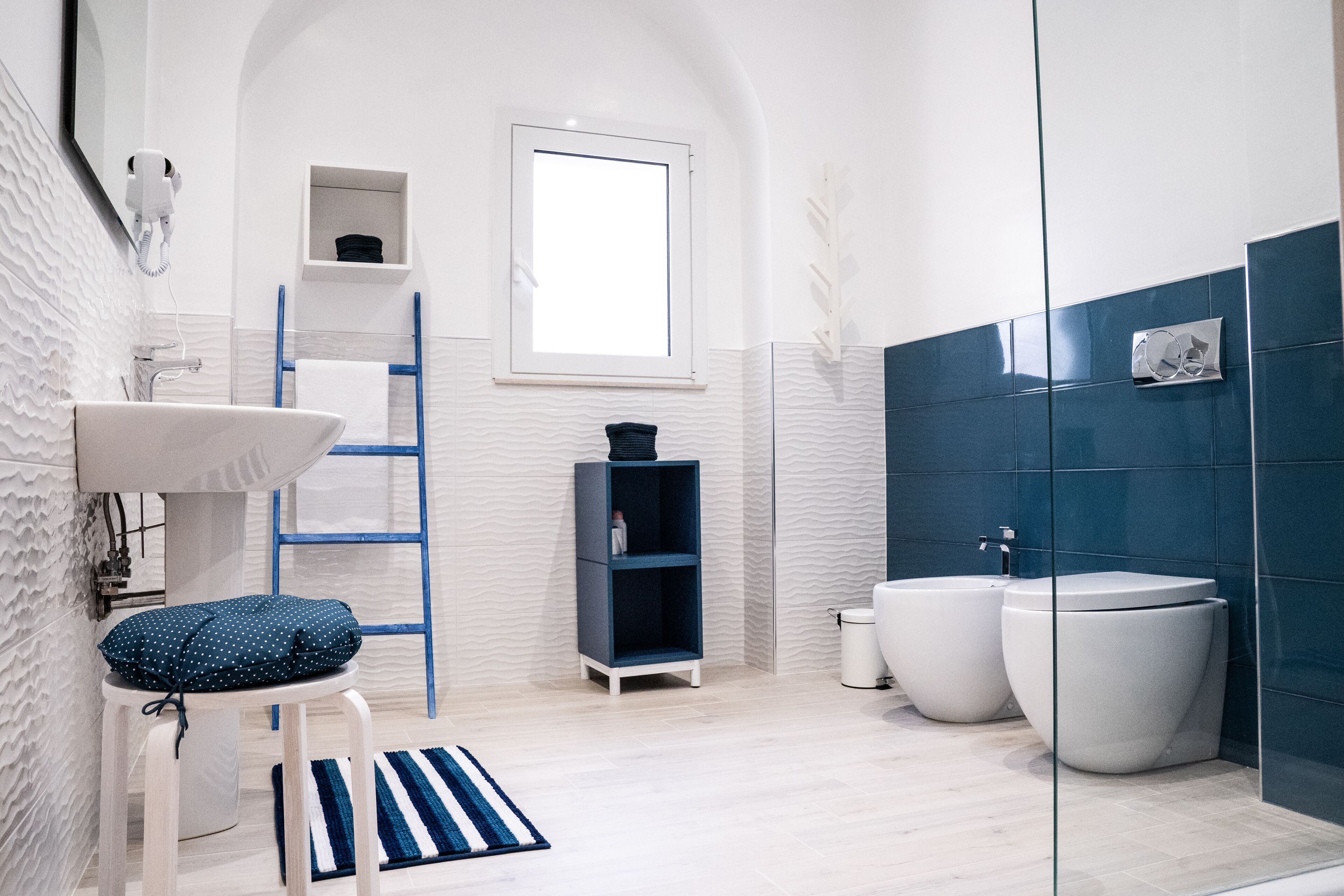 Uma casa de banho moderna com uma pia branca, uma toalha azul, uma sanita branca e uma banheira azul.