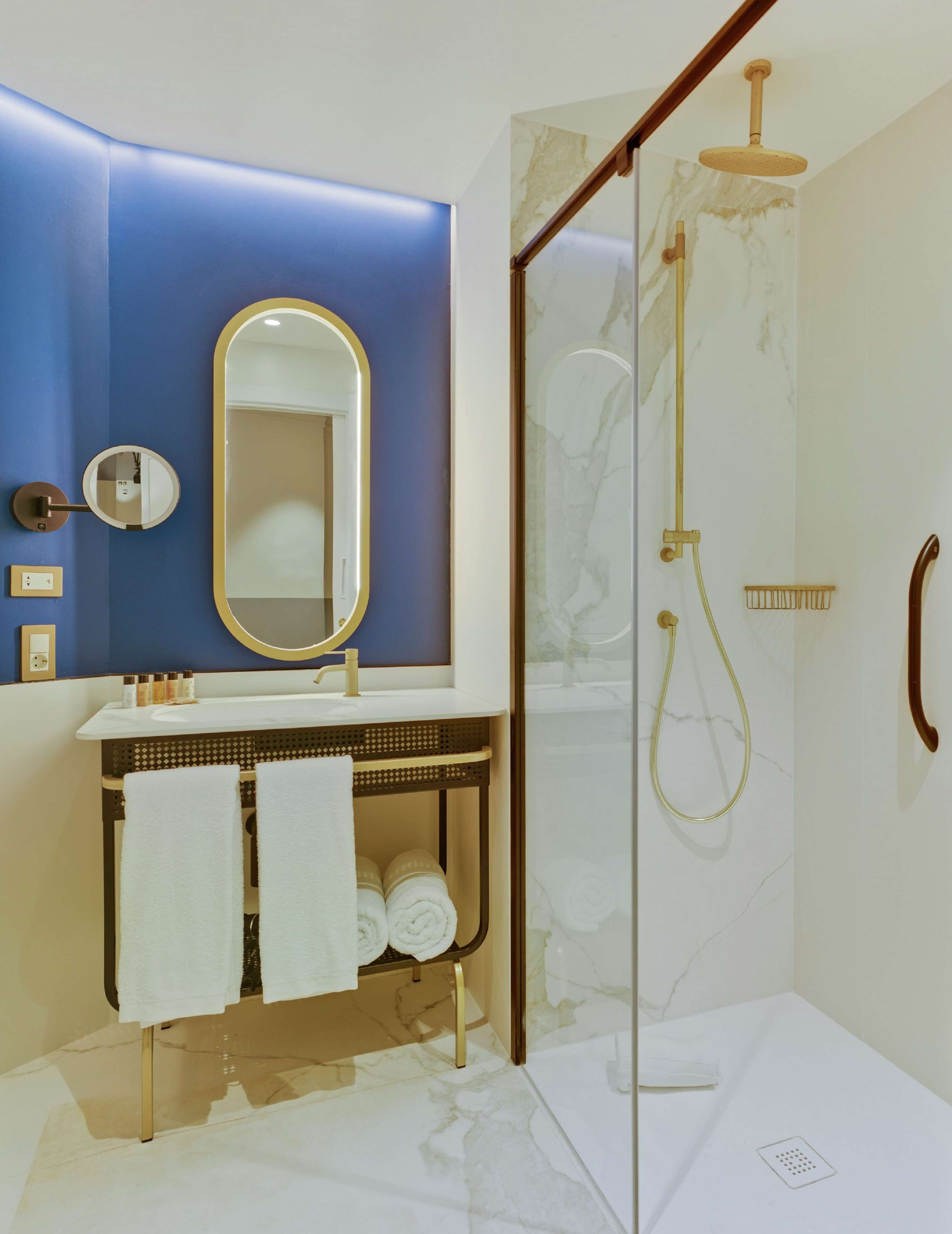 A modern bathroom with a glass-enclosed shower, a vanity with a gold finish, and a blue accent wall.
