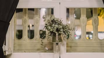 A table with a vase of flowers and a glass, set against a window with decorative railings.