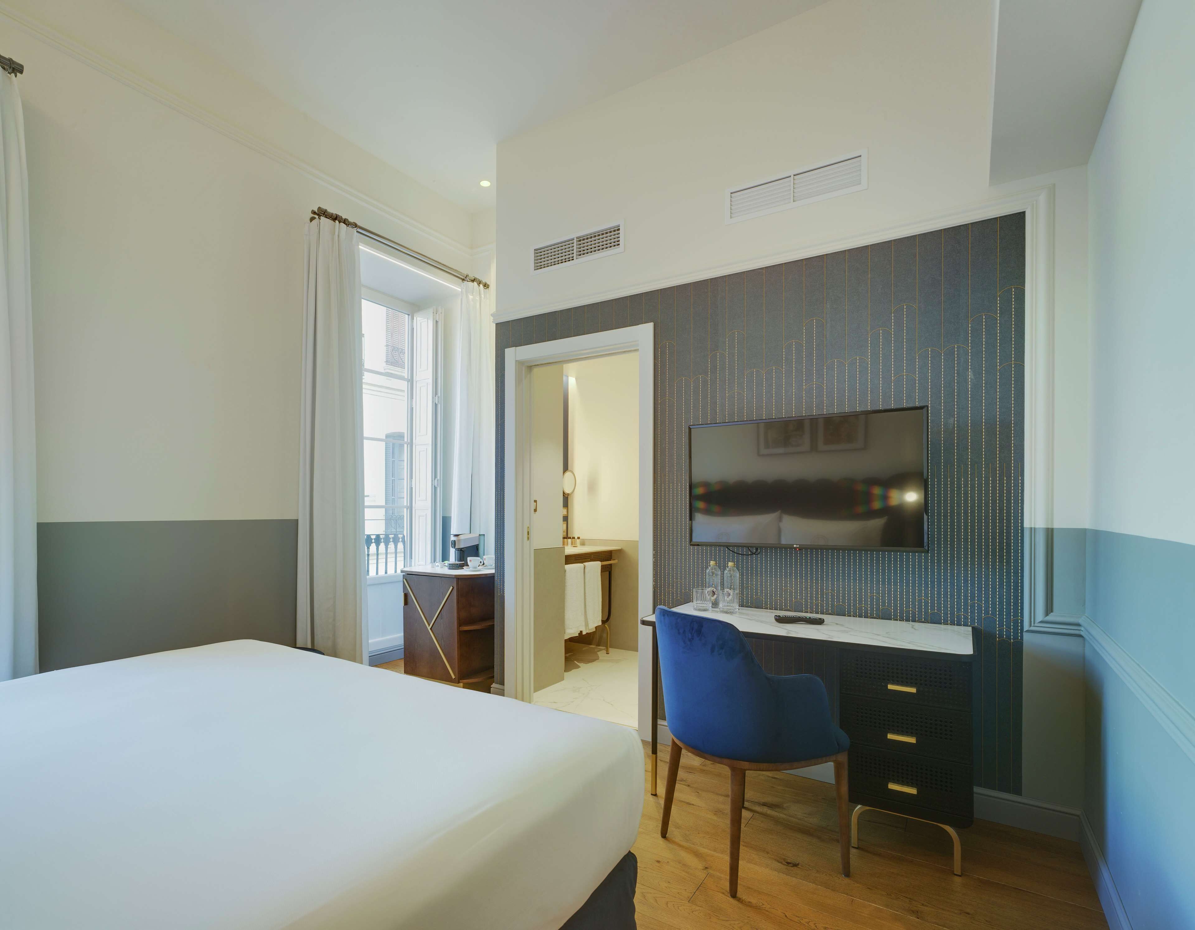 Une chambre d’hôtel avec un lit, un bureau et une chaise, un téléviseur et une salle de bain visible à travers une porte ouverte.