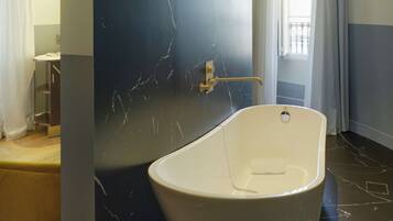 Un bany modern amb una banyera autònoma, una paret de marbre i una finestra amb cortines.
