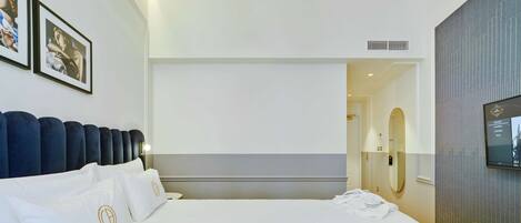 A modern hotel room with a large bed, a TV, and a bathroom visible through an open door.