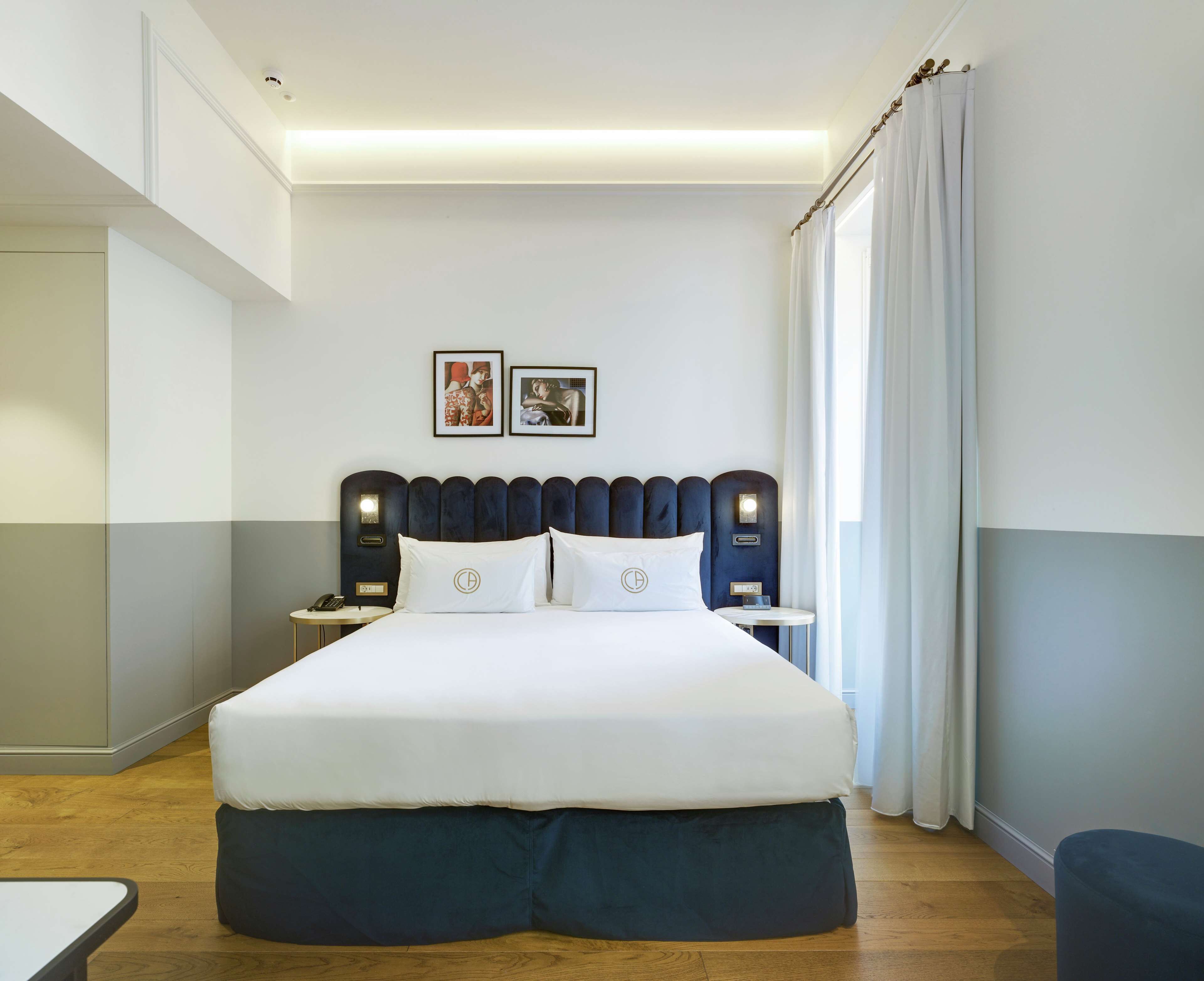 A hotel room with a large bed, two bedside tables, a headboard, and a window with curtains.