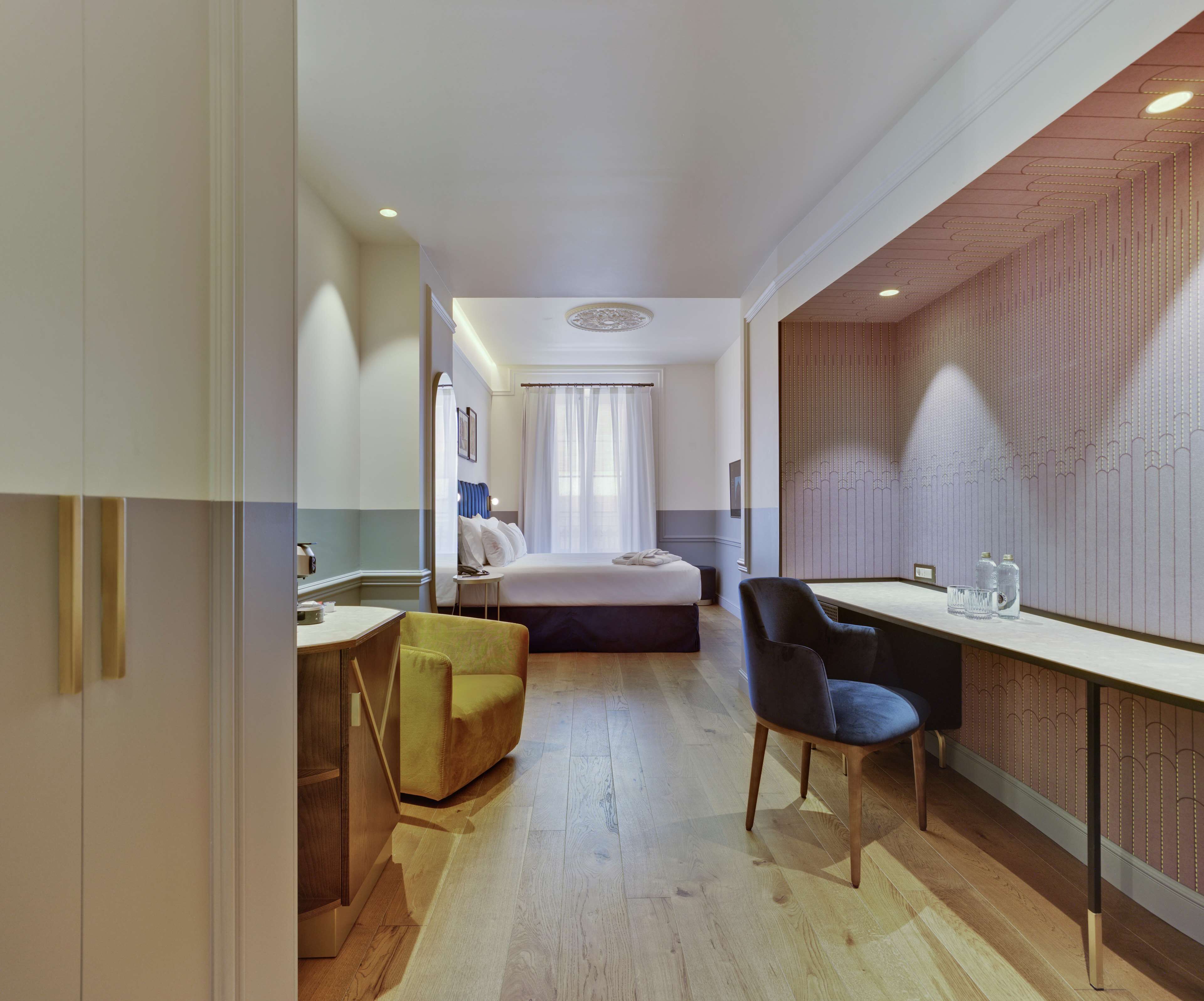 Habitación de hotel con cama, escritorio, silla, mesita y espejo.