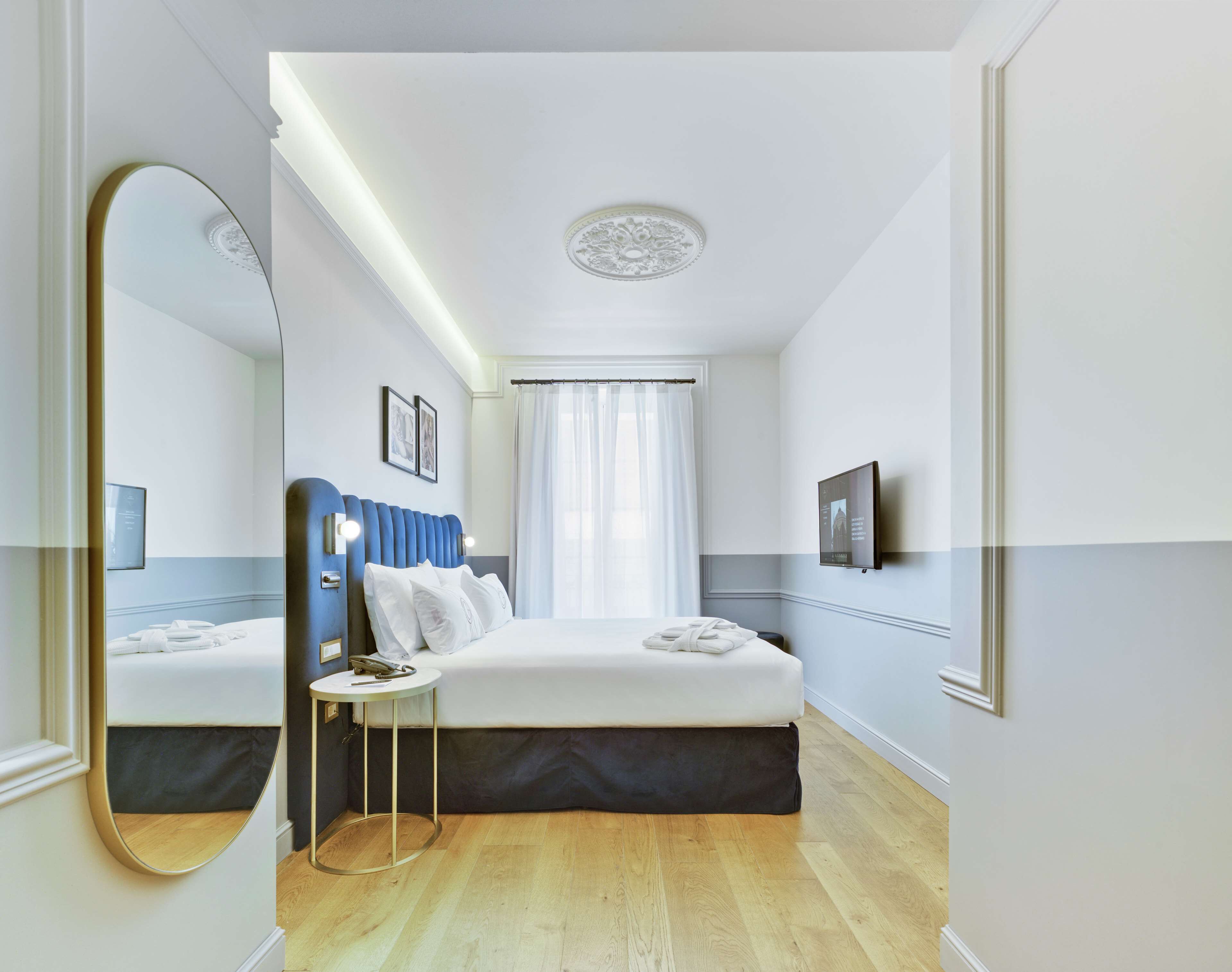 A modern hotel room with a large bed, a bedside table, a mirror, and a television mounted on the wall.