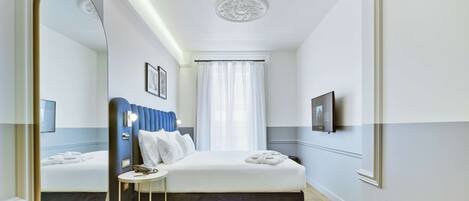 A modern hotel room with a large bed, a bedside table, a mirror, and a television mounted on the wall.