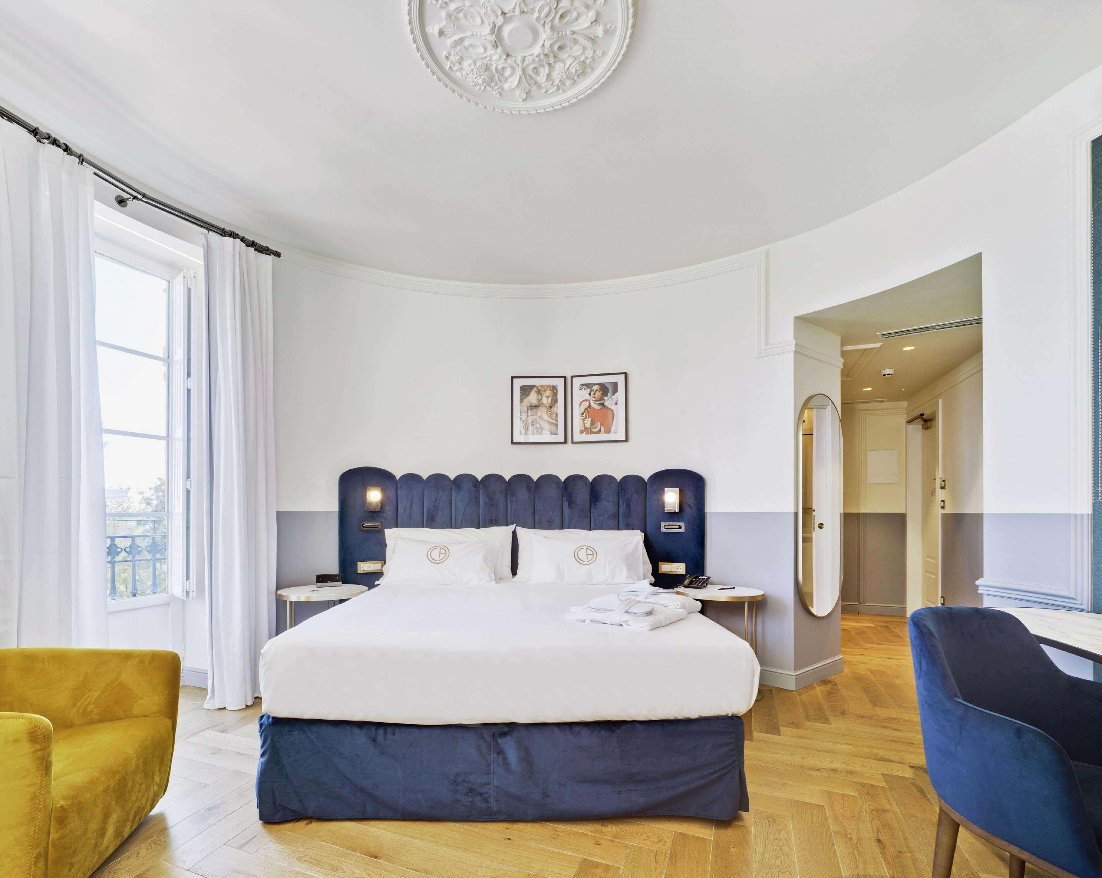 A hotel room with a large bed, a bedside table, a chair, a mirror, and a view of the outdoors.
