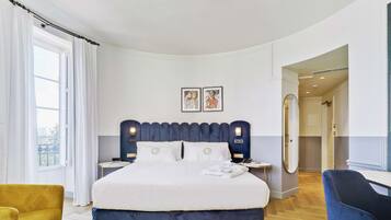 A hotel room with a large bed, a bedside table, a chair, a mirror, and a view of the outdoors.