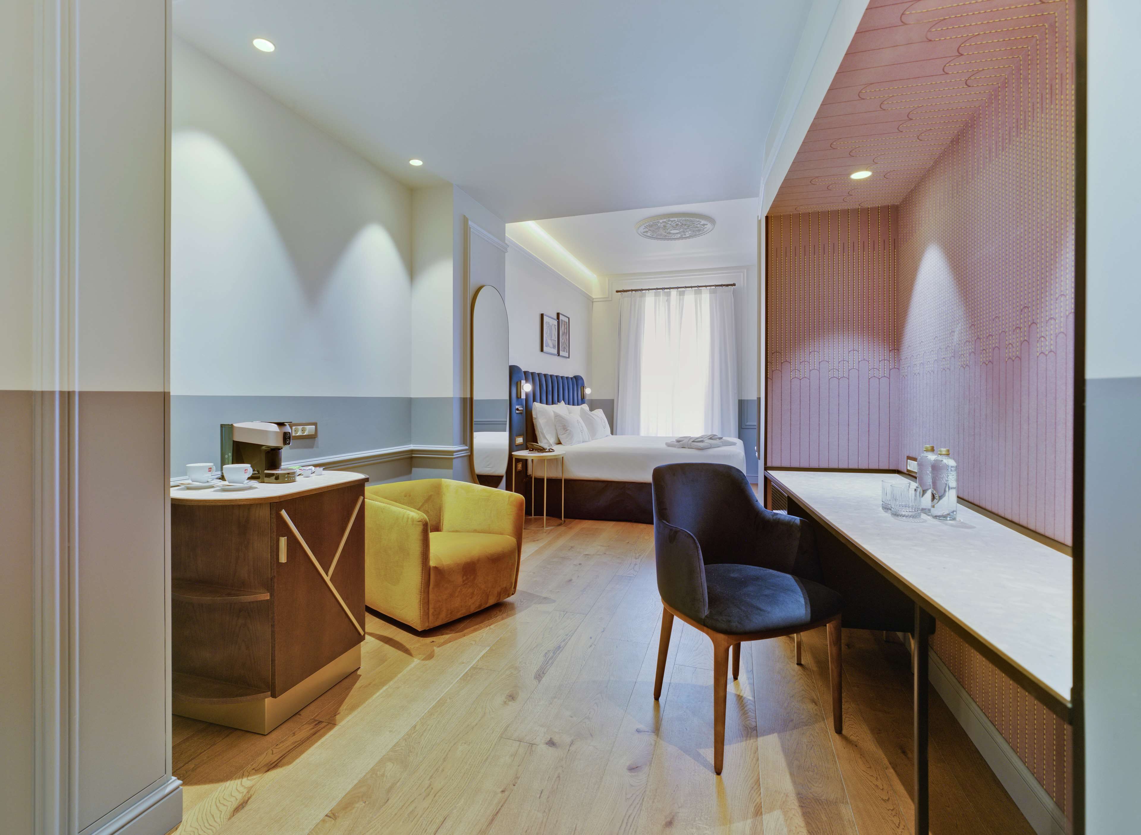 A hotel room with a bed, a desk, a chair, a small table, and a mirror.