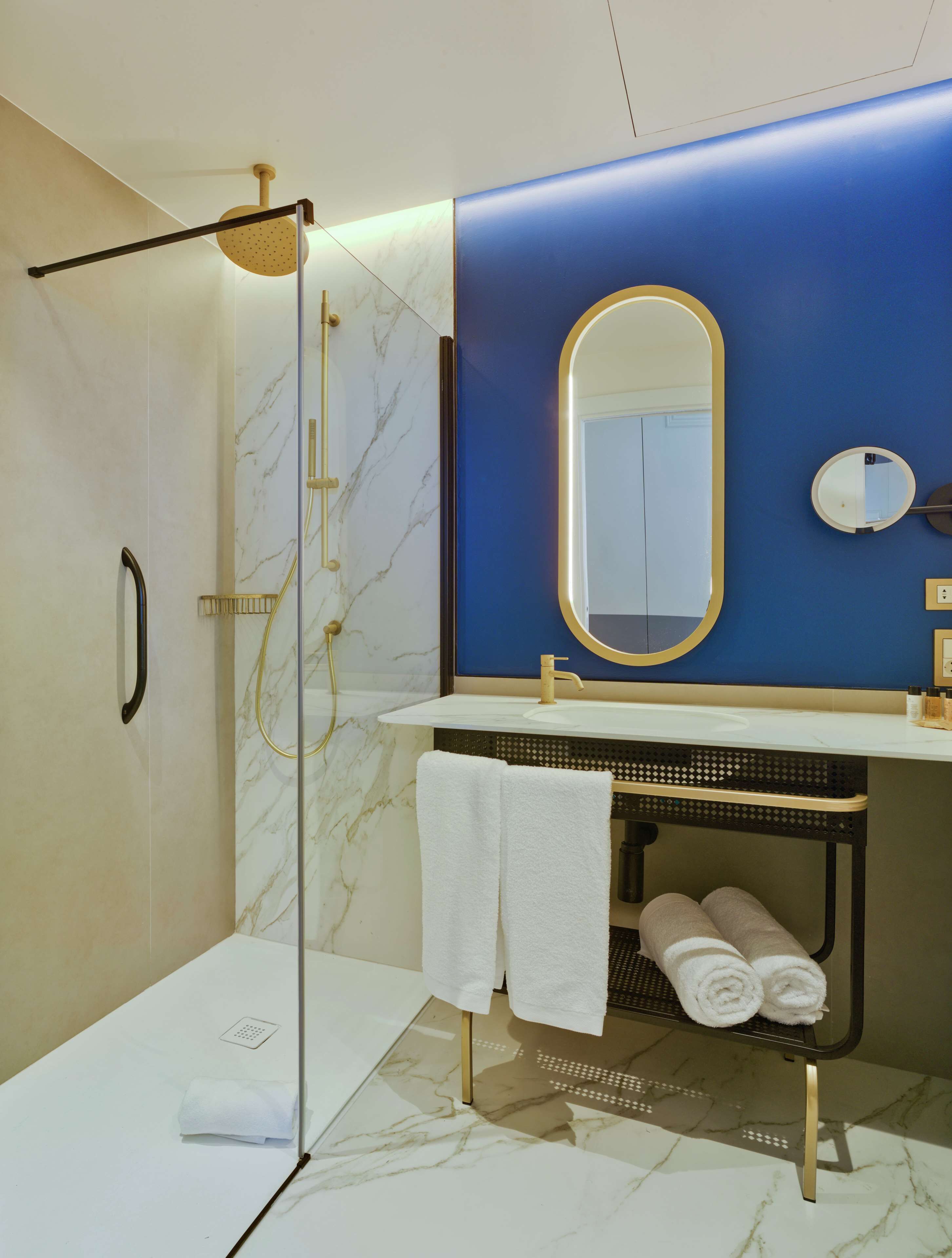 Une salle de bain moderne avec une douche à parois de verre, un meuble-lavabo doté d’un robinet doré et un mur d’accent bleu.