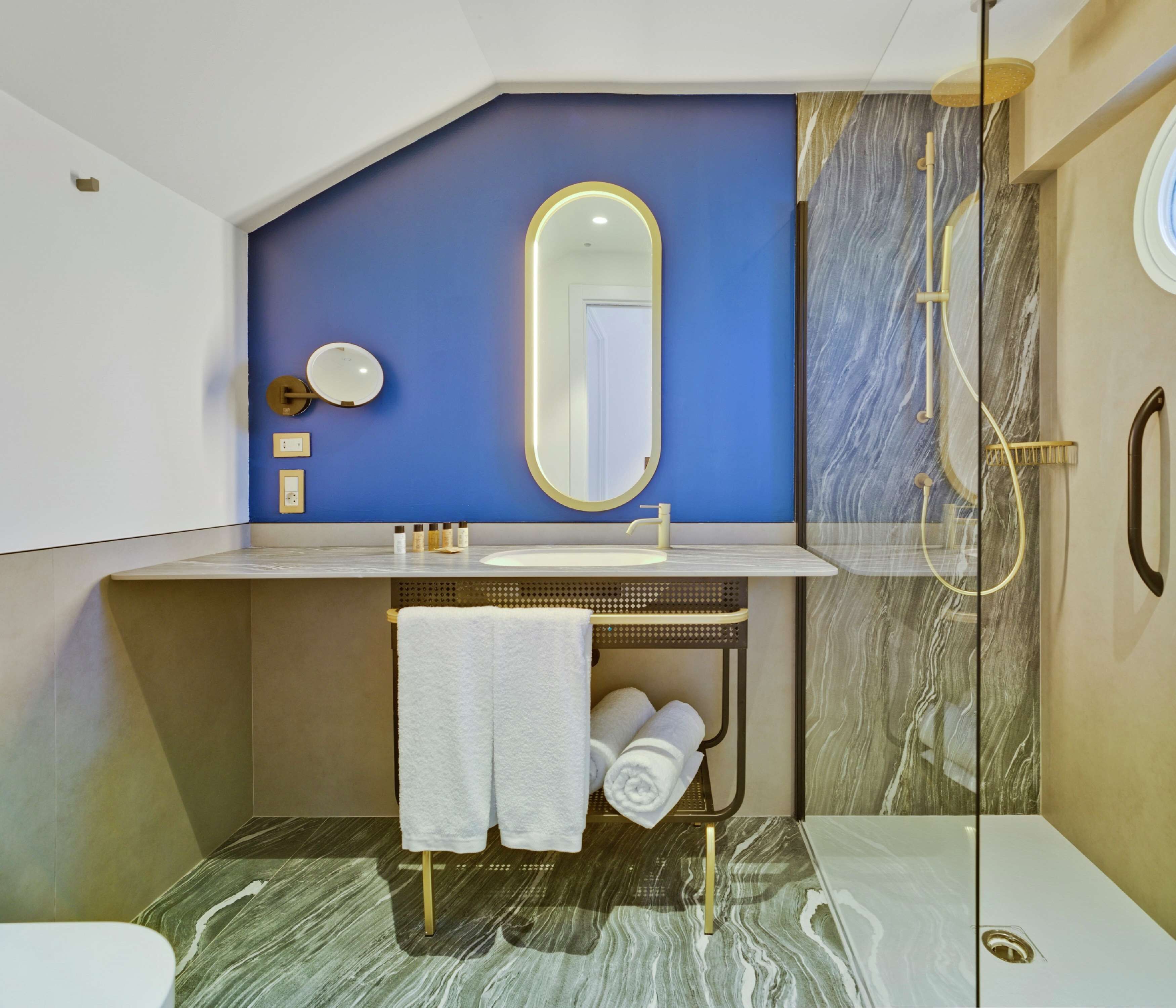 Une salle de bain moderne avec un mur d’accent bleu, un grand miroir, un lavabo et une douche.