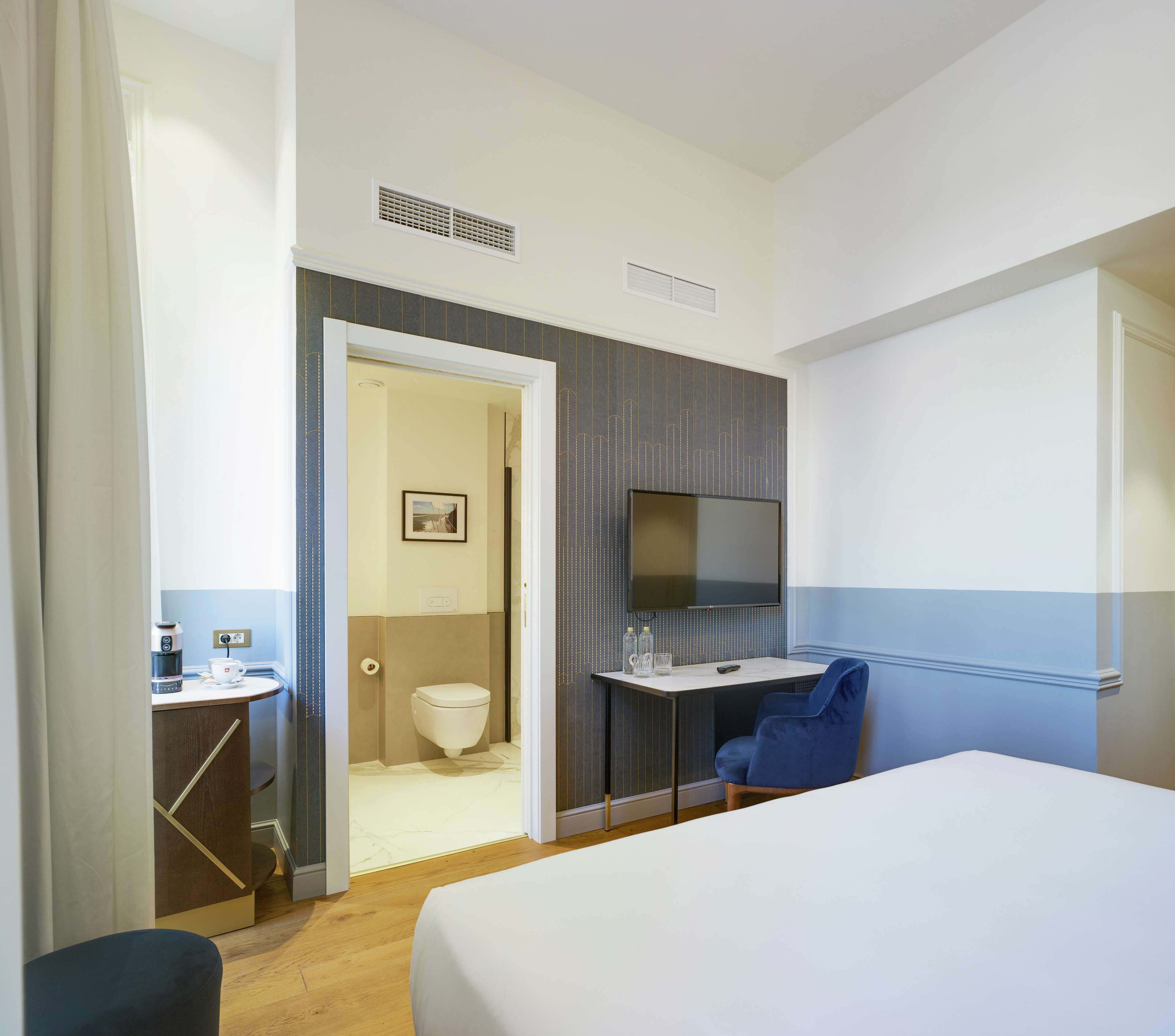 Habitación de hotel con cama, escritorio con silla, televisión y baño visible a través de una puerta abierta.