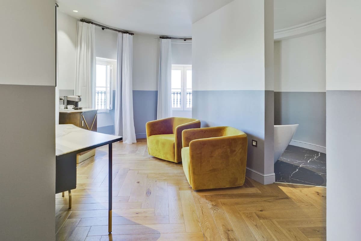 A spacious living area with a wooden floor, a dining table, and two yellow armchairs.