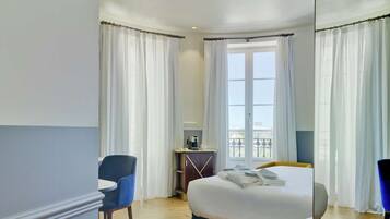 Habitación de hotel con una cama grande, un escritorio, una silla y vistas a la ciudad desde la ventana.