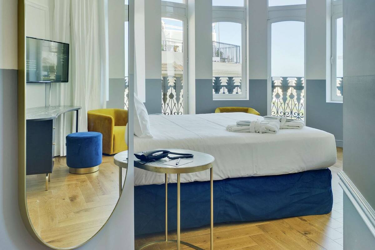 A modern bedroom with a large bed, a round mirror, a small table, and a TV on a stand.
