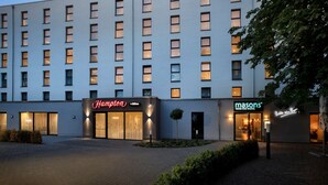 A hotel with a modern facade, featuring two prominent signage for 'Hampton' and 'Masons'.