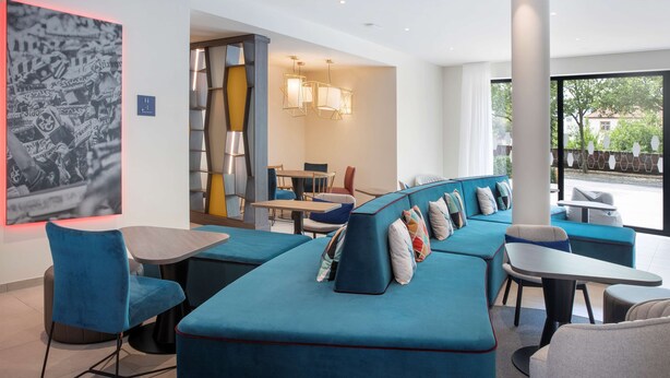 A modern lounge area with blue seating, a large abstract artwork, and a view of the outdoors.