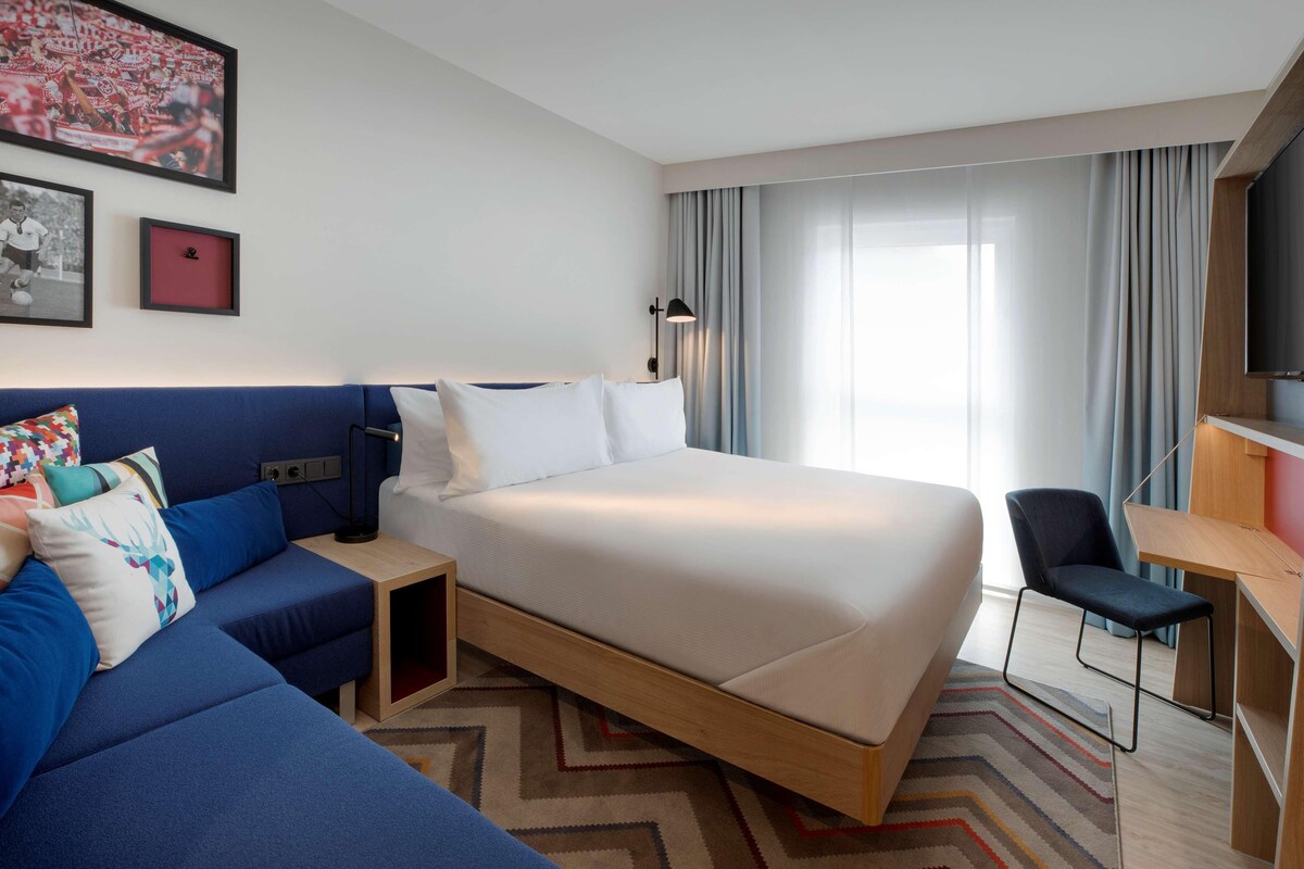 Una habitación de hotel con cama, escritorio, silla, sofá y televisión.