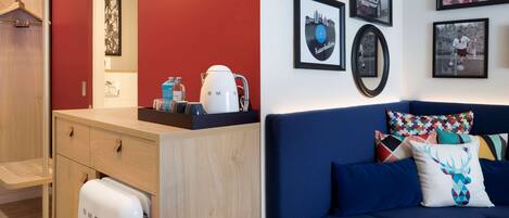 A compact living space with a kitchenette, a sofa with patterned cushions, and wall-mounted artwork.