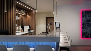 A modern bar area with a long counter, bar stools, and a selection of bottles and glasses.