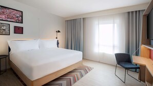 A modern hotel room with a large bed, a desk, and a chair.