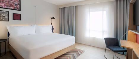 A modern hotel room with a large bed, a desk, and a chair.