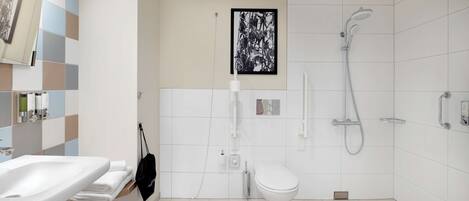 Een moderne badkamer met een witte wastafel, toilet en douche. Er is een handdoekhouder met een zwarte tas en een ingelijst beeld aan de muur.