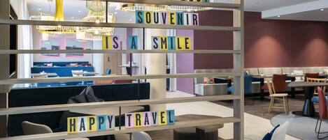A modern hotel lobby with seating areas, a visible reception desk, and a decorative sign with positive messages.