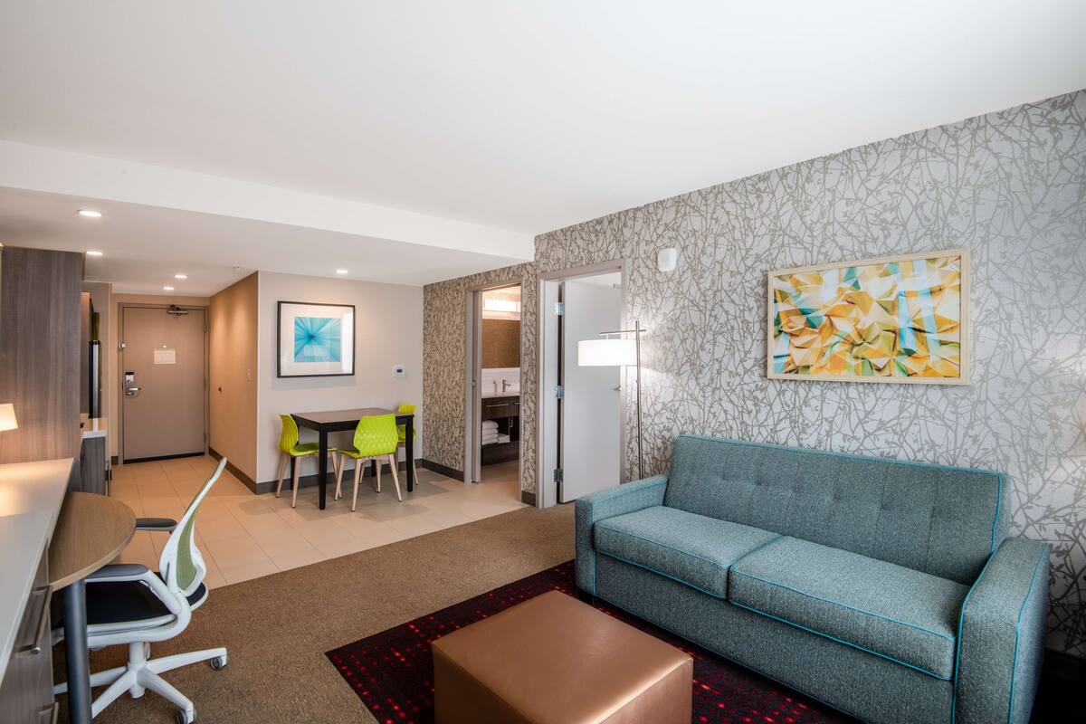 Une chambre d’hôtel moderne comprenant un canapé, une table basse, un bureau avec une chaise et un coin repas avec des chaises.