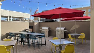 Un patio al aire libre con mesas, sillas, una parrilla y luces colgantes.