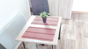 Un pequeño comedor con una mesa, dos sillas, una planta en maceta y un mueble en el fondo.