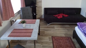 Una sala de estar con un sofá, una mesa con una planta, un televisor y un cuadro en la pared.