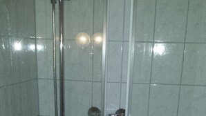 Un box de ducha con puerta de vidrio, un cabezal de ducha de mano y una llave instalada en la pared.
